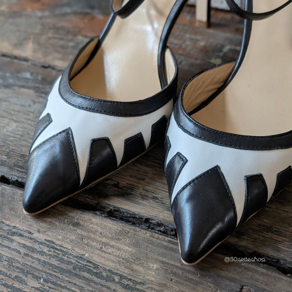 Décolleté con tacco di media altezza realizzata in nappa nero con inserti geometrici in nappa panna con punta sfilata e cinturino alla caviglia.