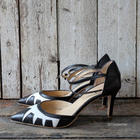 Décolleté con tacco di media altezza realizzata in nappa nero con inserti geometrici in nappa panna con punta sfilata e cinturino alla caviglia.
