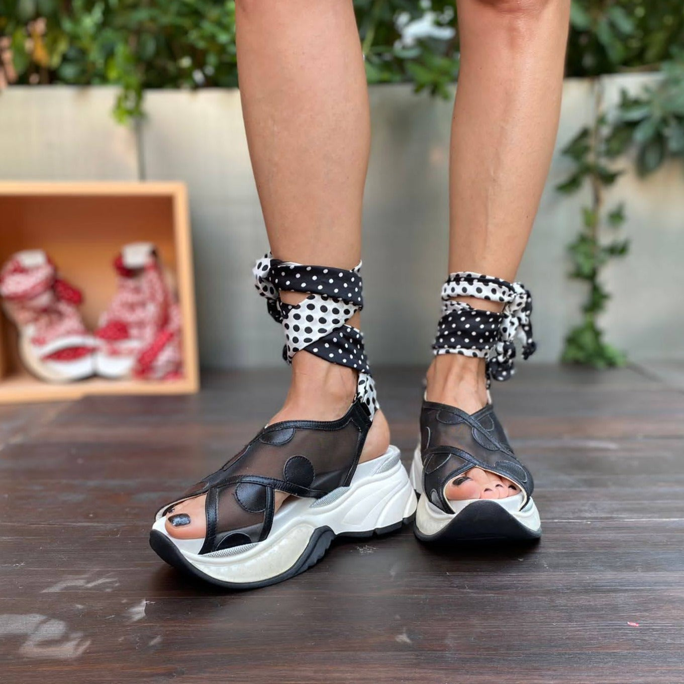 Sneakers chunky o sandalo con zeppa in pelle e rete nera chiuso alla caviglia da un foulard in seta bianco e nero che si intreccia sul piede e si avvolge alla caviglia. 