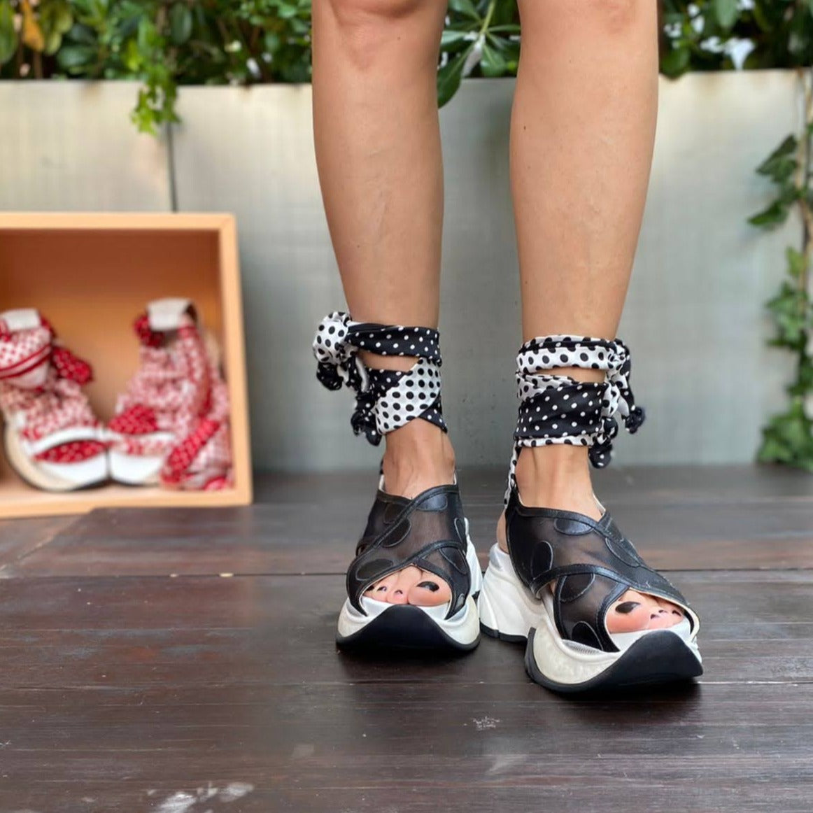 Sneakers chunky o sandalo con zeppa in pelle e rete nera chiuso alla caviglia da un foulard in seta bianco e nero che si intreccia sul piede e si avvolge alla caviglia. 