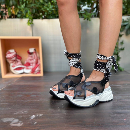 Sneakers chunky o sandalo con zeppa in pelle e rete nera chiuso alla caviglia da un foulard in seta bianco e nero che si intreccia sul piede e si avvolge alla caviglia. 