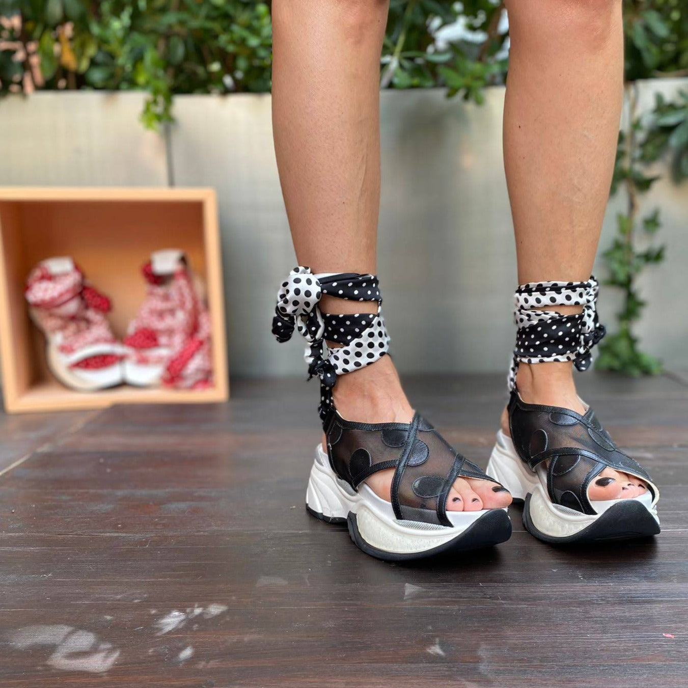 Sneakers chunky o sandalo con zeppa in pelle e rete nera chiuso alla caviglia da un foulard in seta bianco e nero che si intreccia sul piede e si avvolge alla caviglia. 