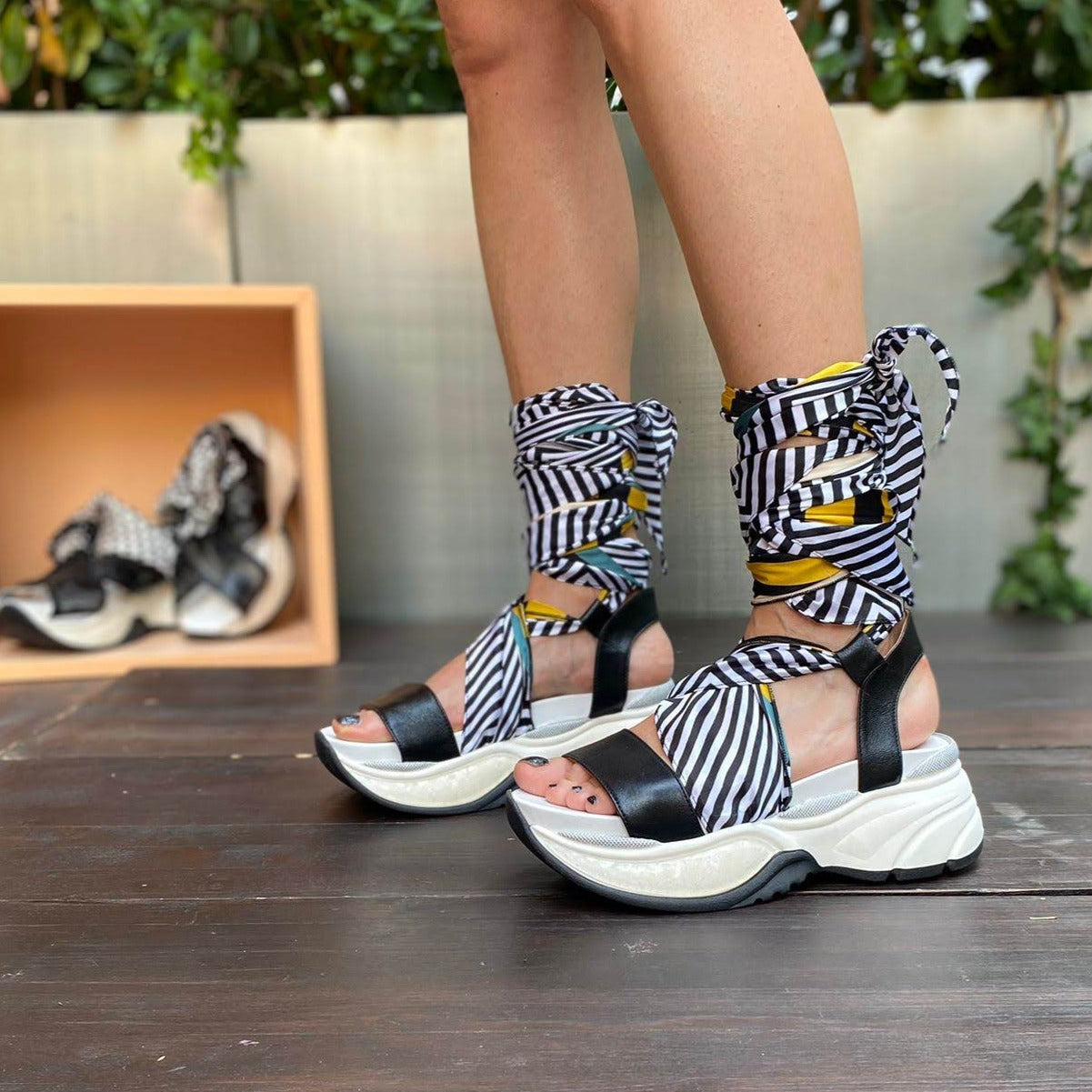 Sneakers chunky o sandalo con zeppa in morbida pelle nera con foulard di seta montato tra suola e tomaia, che si intreccia sul piede e si avvolge alla caviglia. 