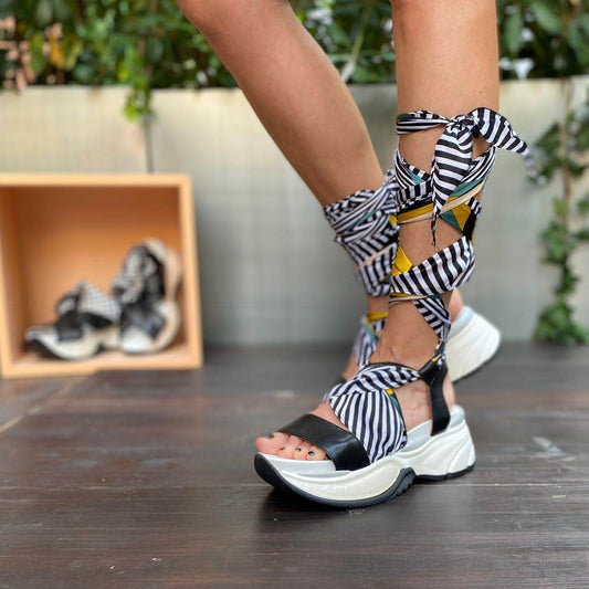 Sneakers chunky o sandalo con zeppa in morbida pelle nera con foulard di seta montato tra suola e tomaia, che si intreccia sul piede e si avvolge alla caviglia. 