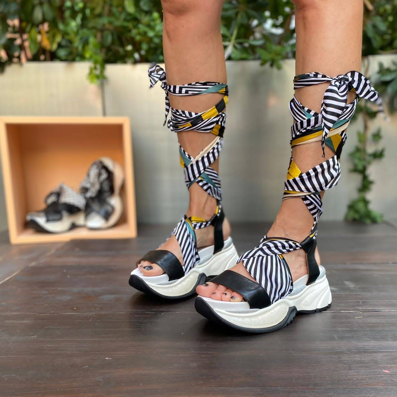 Sneakers chunky o sandalo con zeppa in morbida pelle nera con foulard di seta montato tra suola e tomaia, che si intreccia sul piede e si avvolge alla caviglia. 